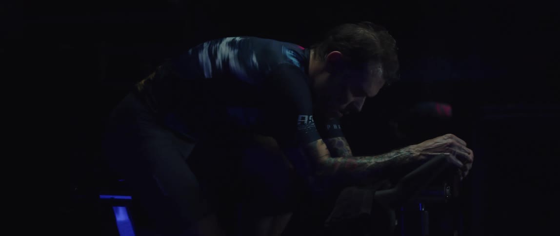 Athletic man wearing a cycling jersey riding a stationary bike in a dark room
