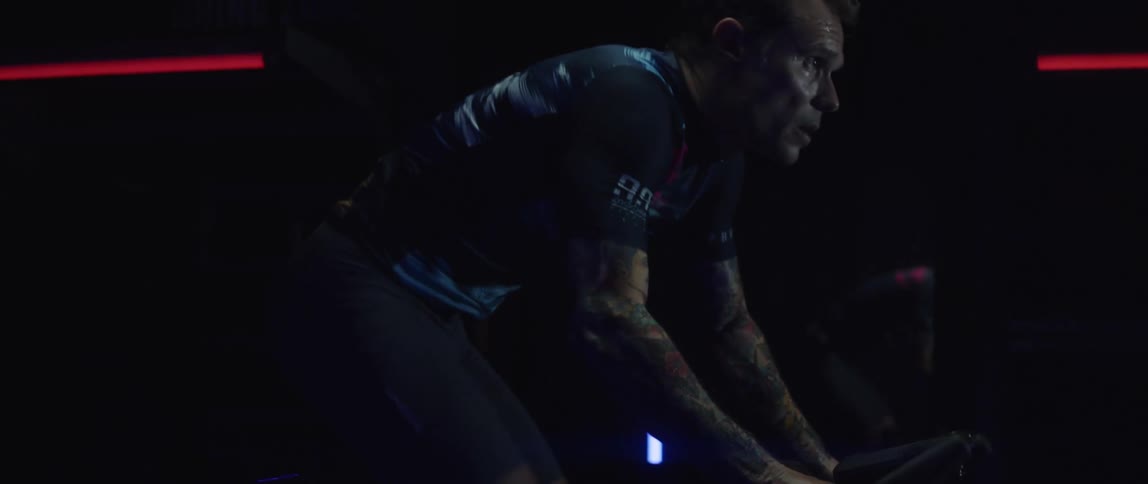 A man exercises on an exercise bike in a dark room