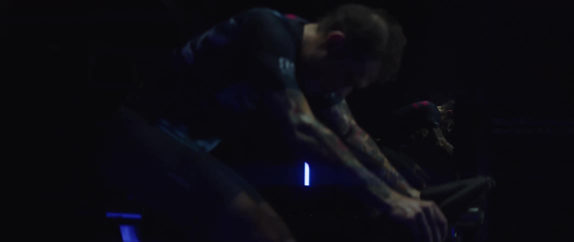 Man pedaling on a static bicycle inside a dimly lit room against a dark background