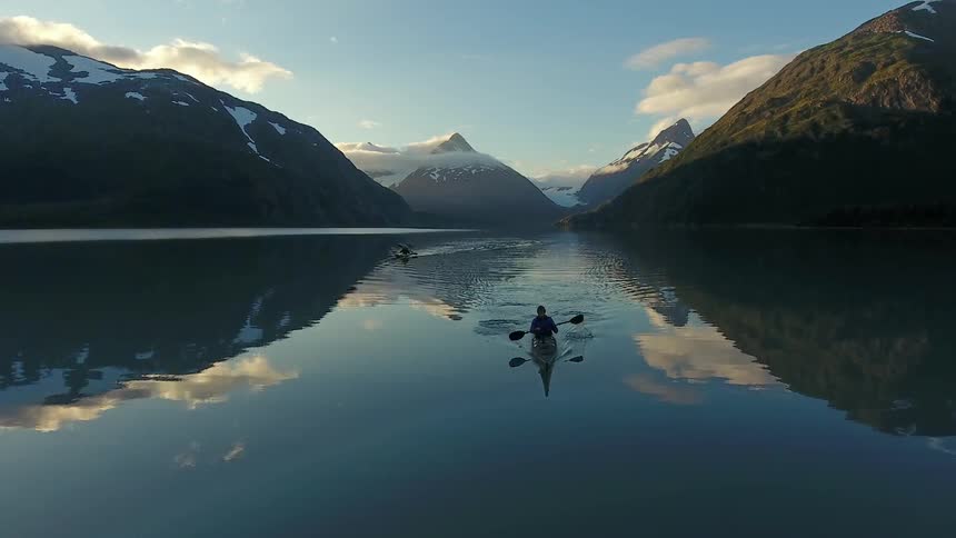A man is rowing in the lake near a mountain range