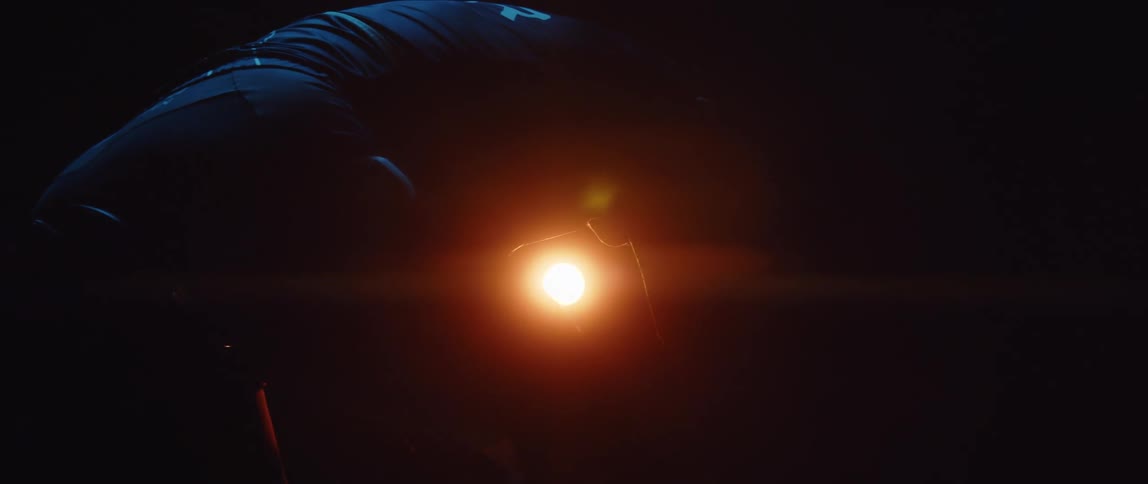 Silhouette of a man pedaling a static bicycle inside a dimly lit room under a spotlight