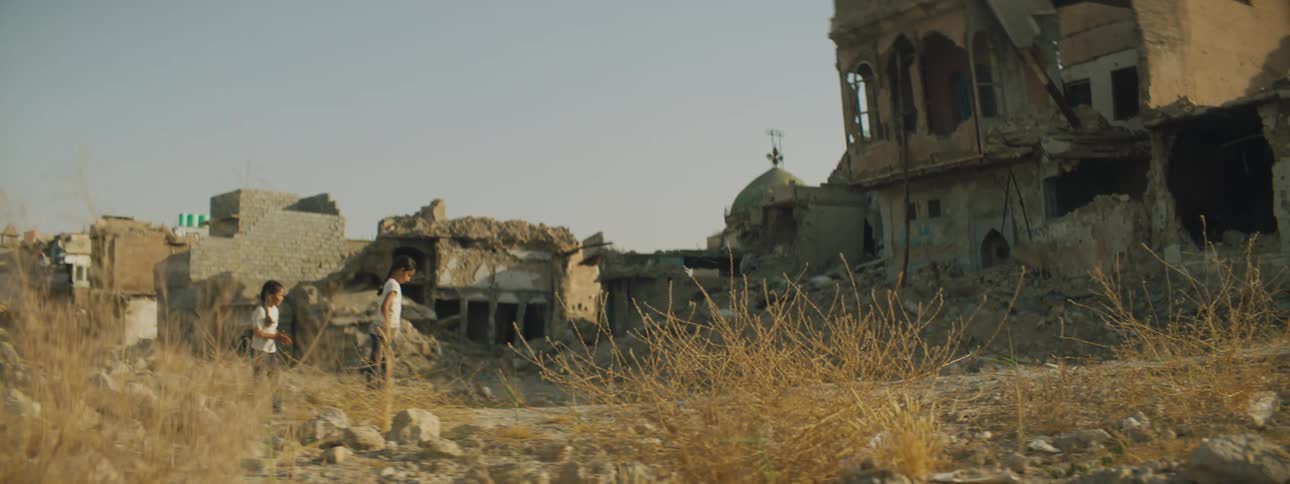 Two children play outside of the ruined town