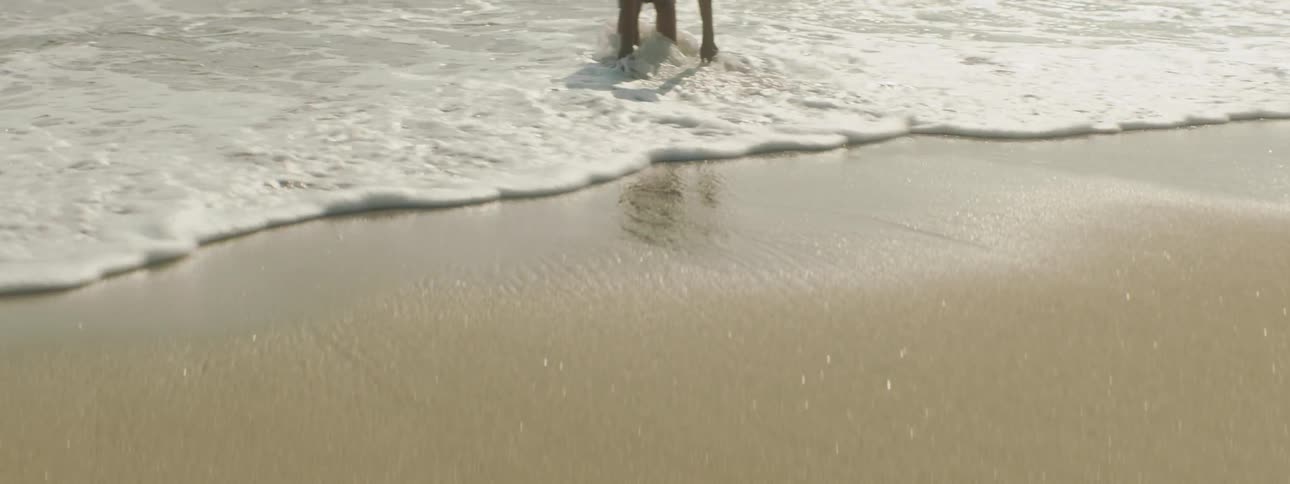 A boy in a swimsuit playing in ocean waves on a sandy beach in the daytime