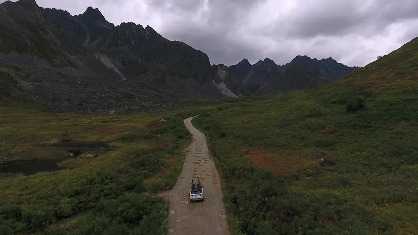 A car travels slowly on a dirt road near a mountain pass