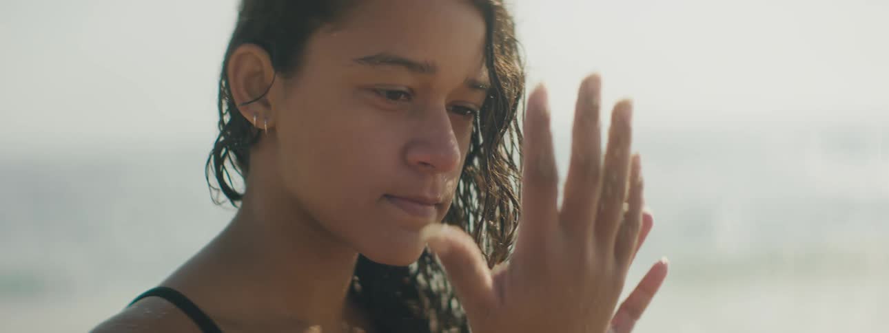 A young woman sitting on the beach on a sunny day examines her hands
