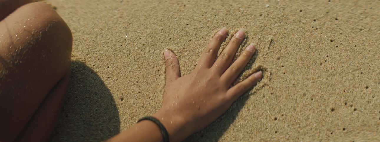 Female youth gently places her hand on top of wet sand and then moves her hand back and forth slightly in order to make a hand imprint