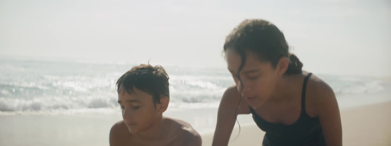 A boy and a girl on the beach digging in the sand with the sky and clouds in the background