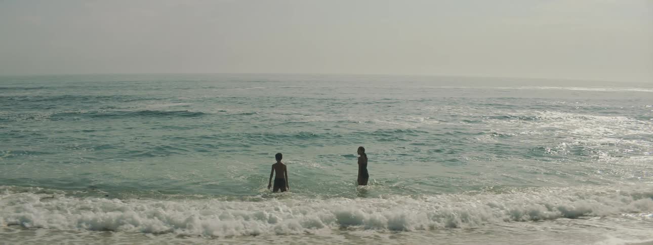 A young boy and girl wade and splash in the ocean
