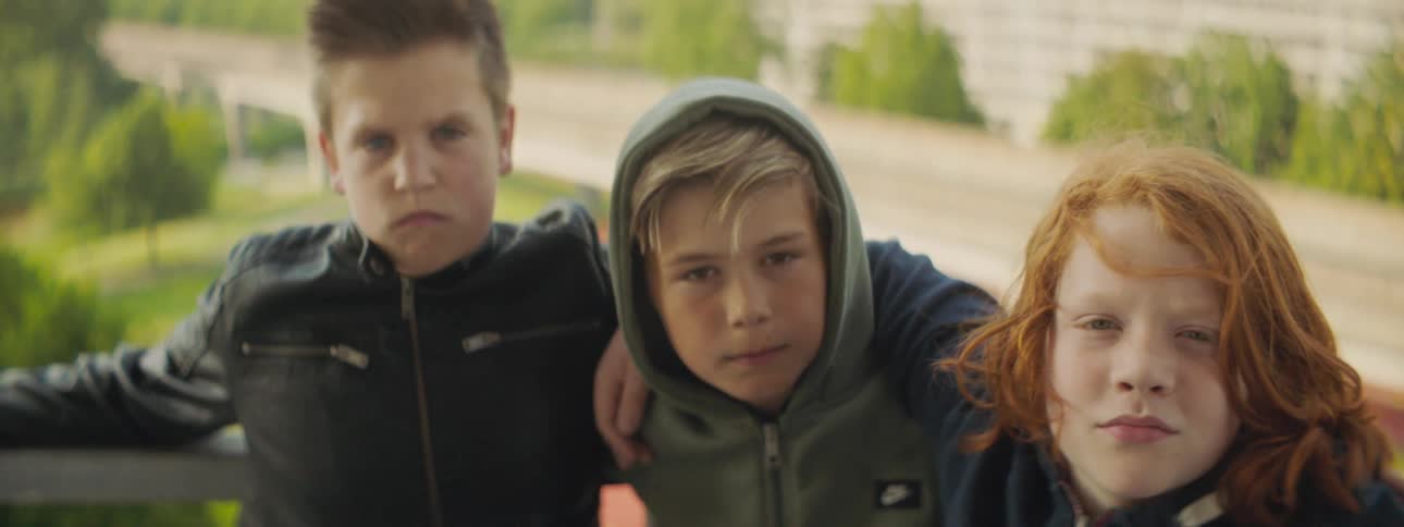 Three kids stand close together against rail with bridge in background