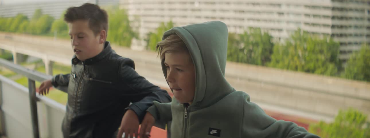 Two young boys hanging out by a railing on a building in the city