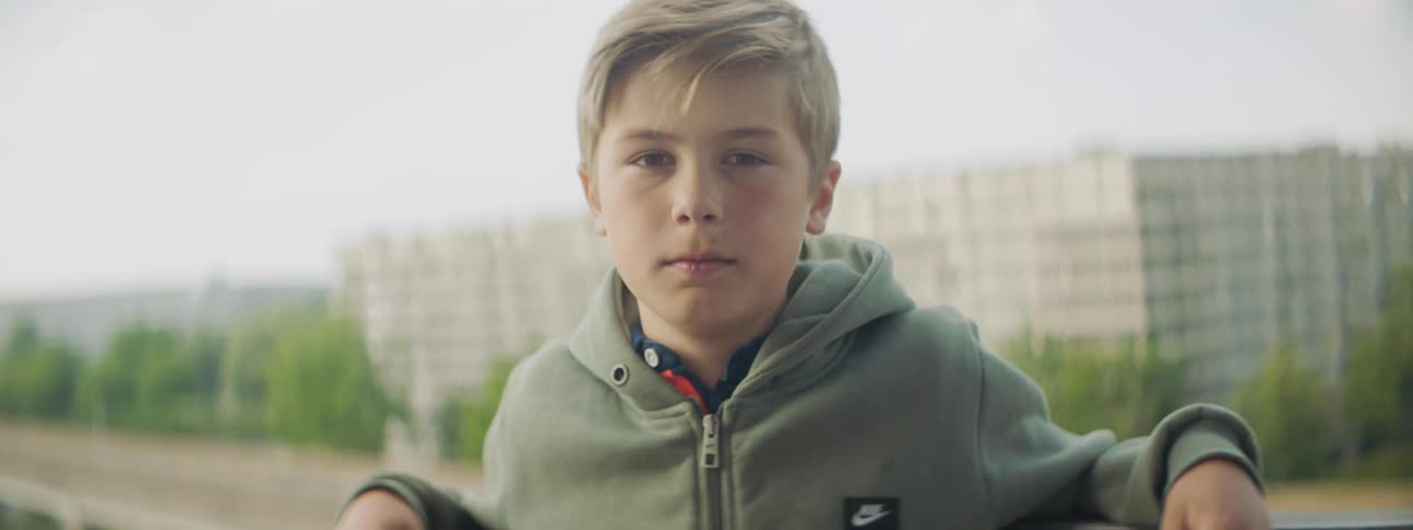 A boy with buildings trees the sky and clouds in the background