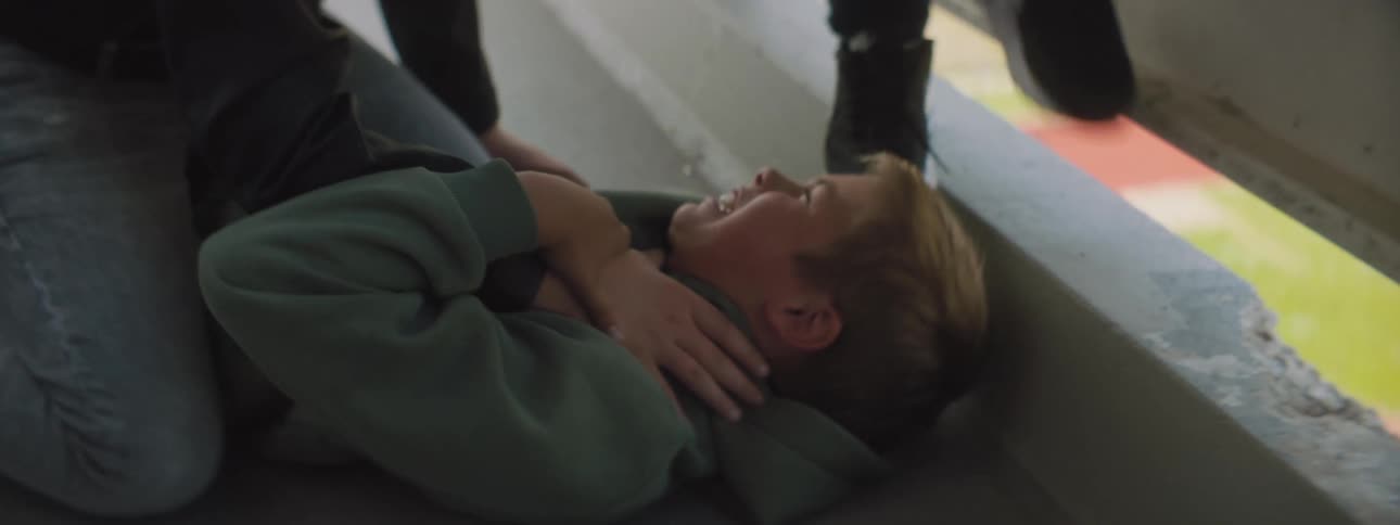 Boy is being bullied on floor near sports field visible through gap