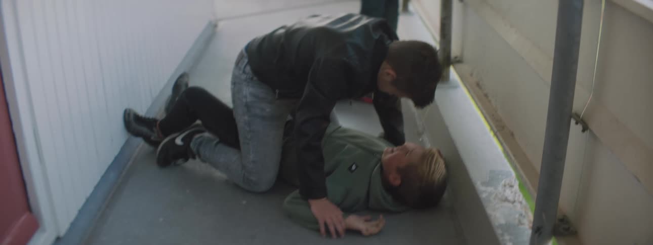 Boy pins another on concrete bullying him while another watches