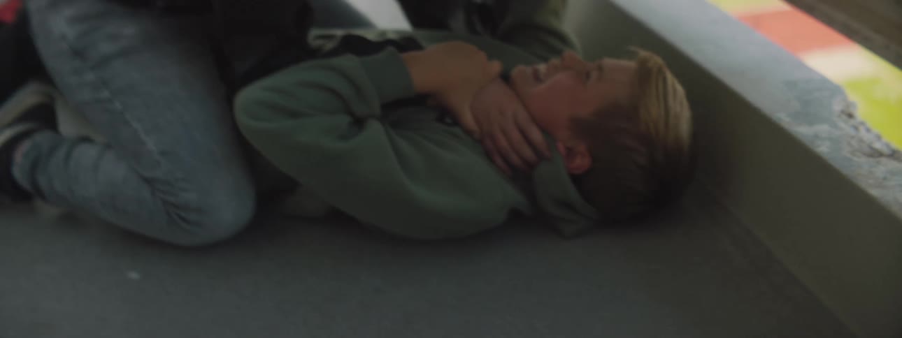 Boys bully another holding him down on concrete in outdoor walkway over sports field