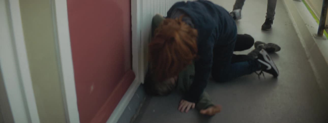 A boy beats up on another boy in a corridor as another boy stands back and watches