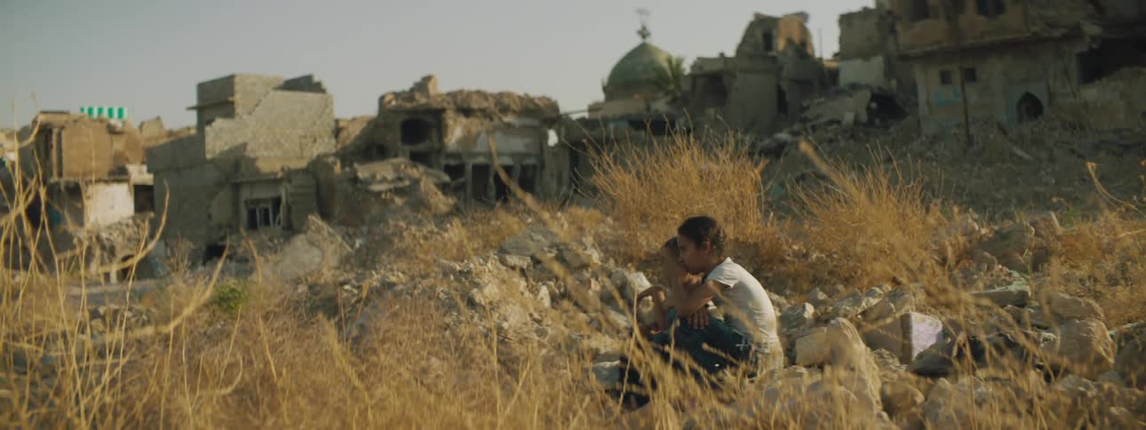 Two young boys sit in a field on the outskirts of a village