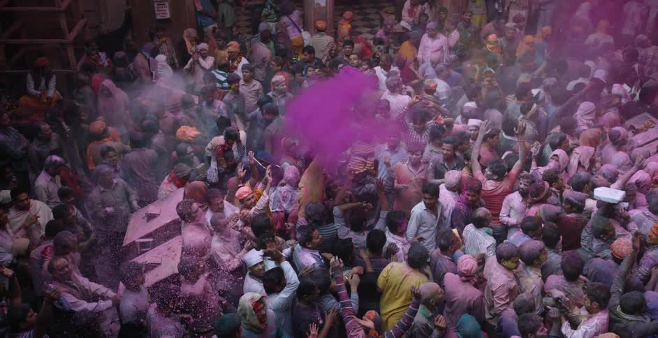 A large crowd of people celebrate and throw colored dust