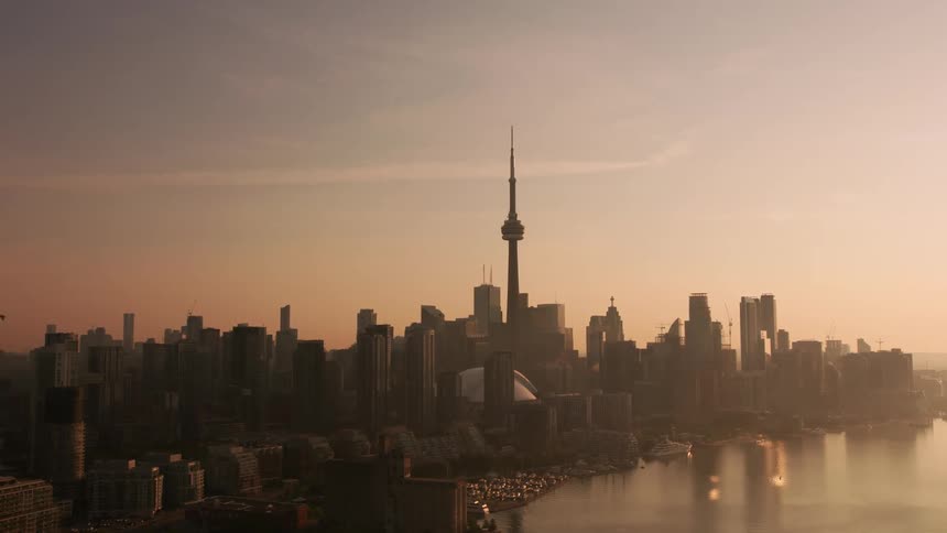 The cn tower standing above the toronto city skyline and harbor at sunrise