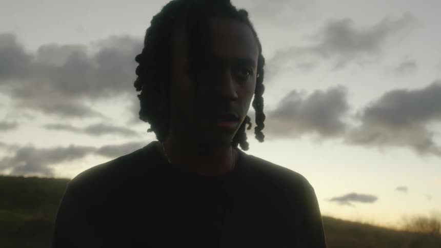 A teenager with dreadlocks standing in a field at dusk