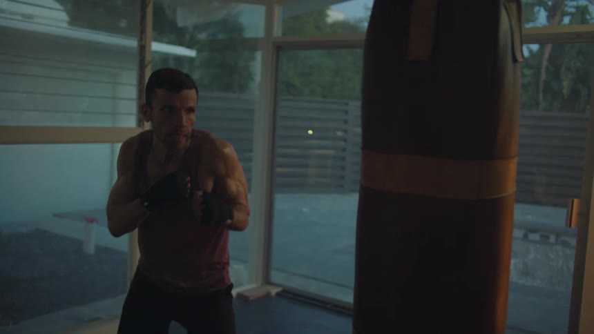 A man works out hitting a hanging heavy bag in his home