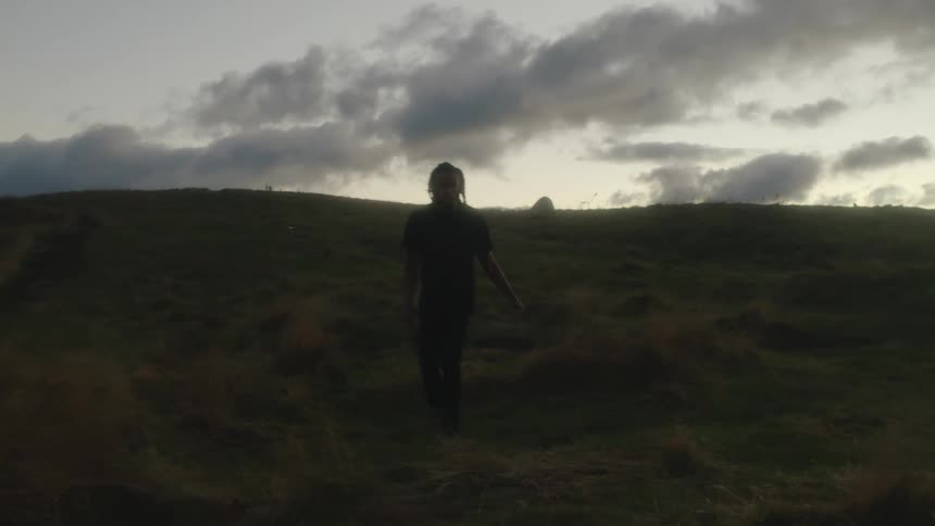A man appears confused as he raises his arms while walking through hilly ground