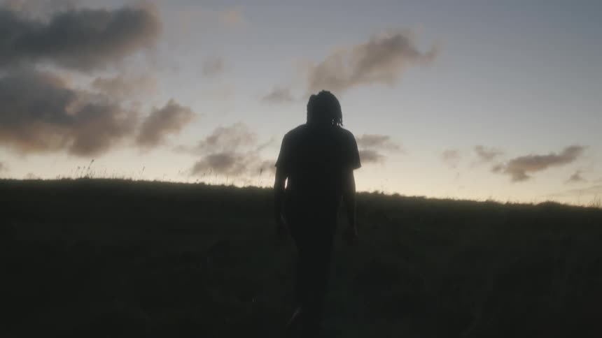 A young black man is walking outside in the forest around the day time