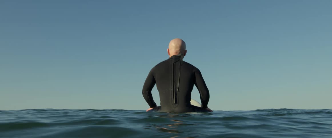 A man sitting on his surfboard looking out at the ocean and horizon
