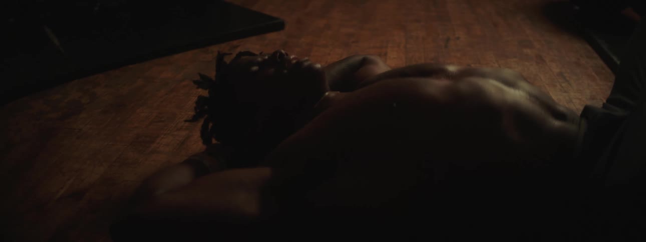 A shirtless man breathing heavily while lying on a wood floor