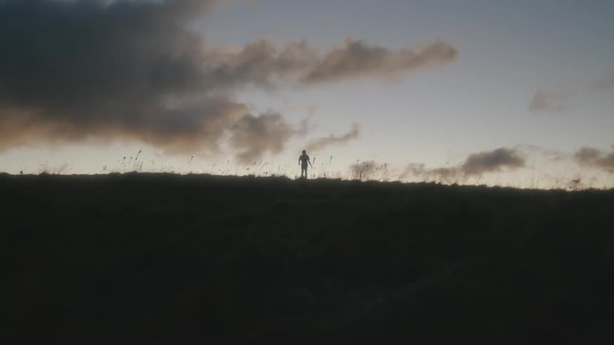 The silhouette of a person walking across a hill in the countryside in the evening