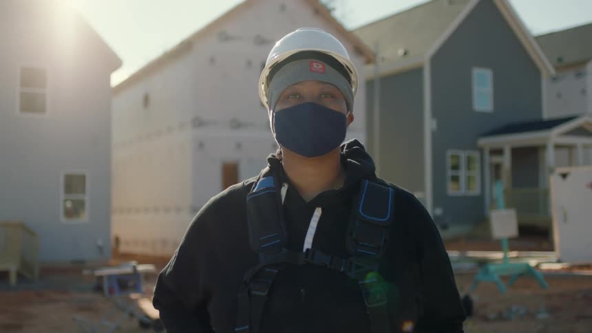 A woman wearing a hardhat is standing in front of homes under construction