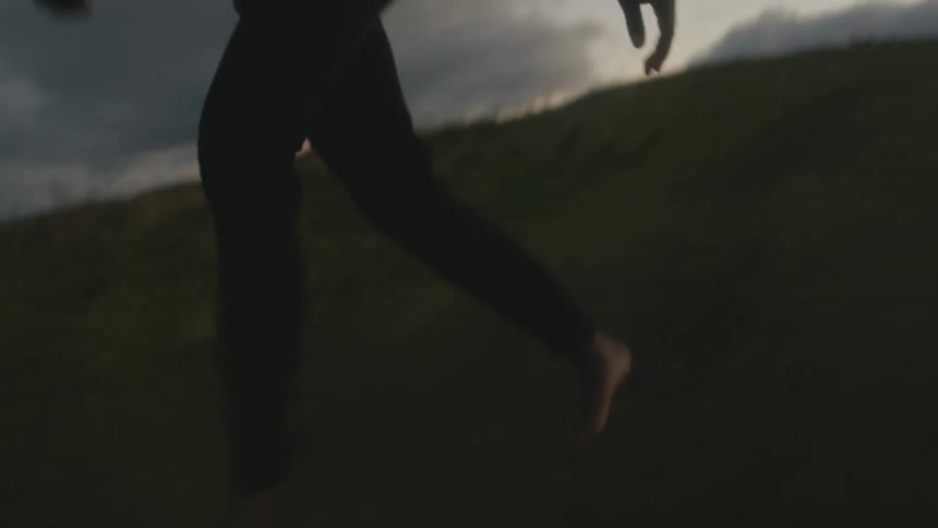 A barefoot person stumbling while walking on a hill at dusk