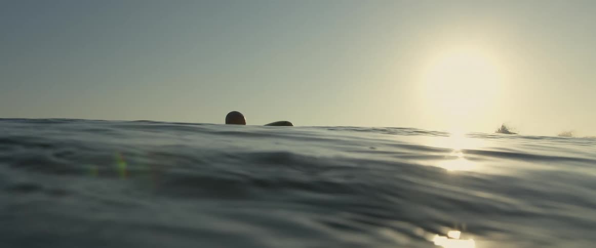 Male surfer wearing wet suit hand paddles surfboard away from shore on a sunny day