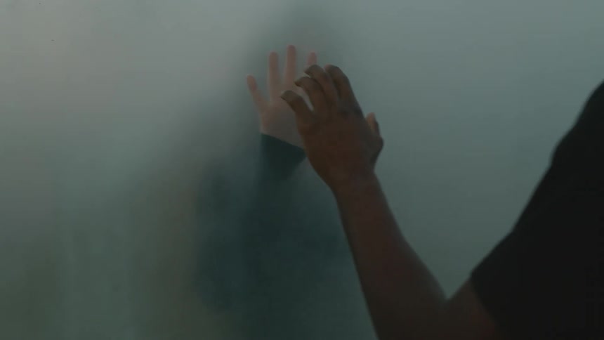 Two people are touching hands through a foggy window