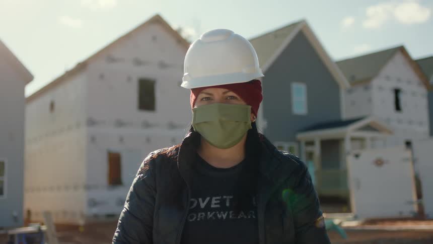 Woman wearing face mask and hardhat stand in front of home construction site