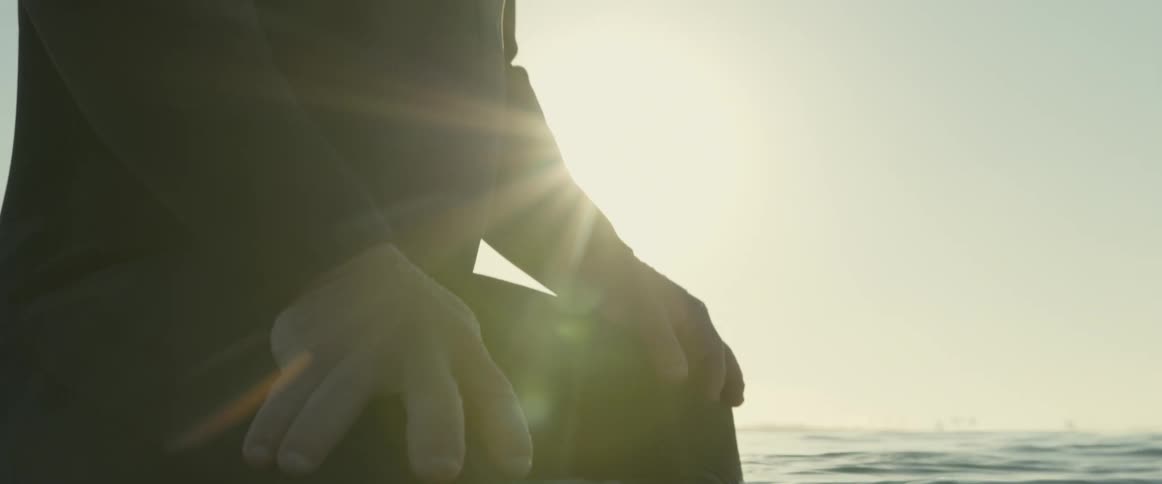 Person wearing wet suit sits on water on sunny day