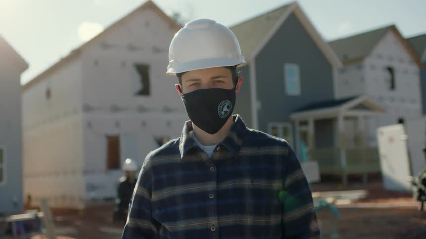 Construction worker wearing a black face mask and white hardhat helmet looking at the camera