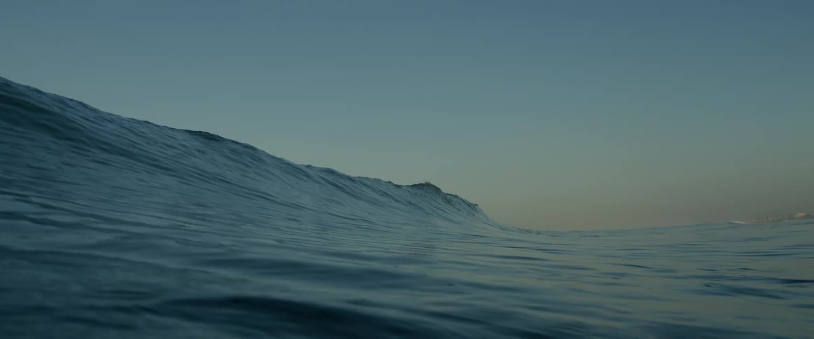 A large ocean wave flowing towards land at dawn