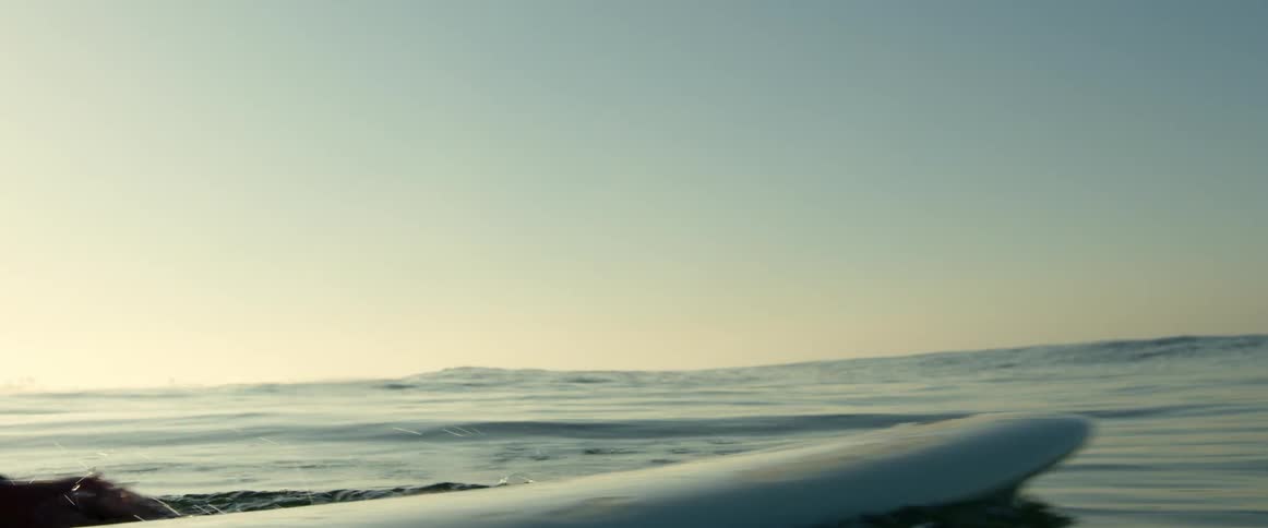 A man paddles out on a surfboard cutting through calm ocean surface