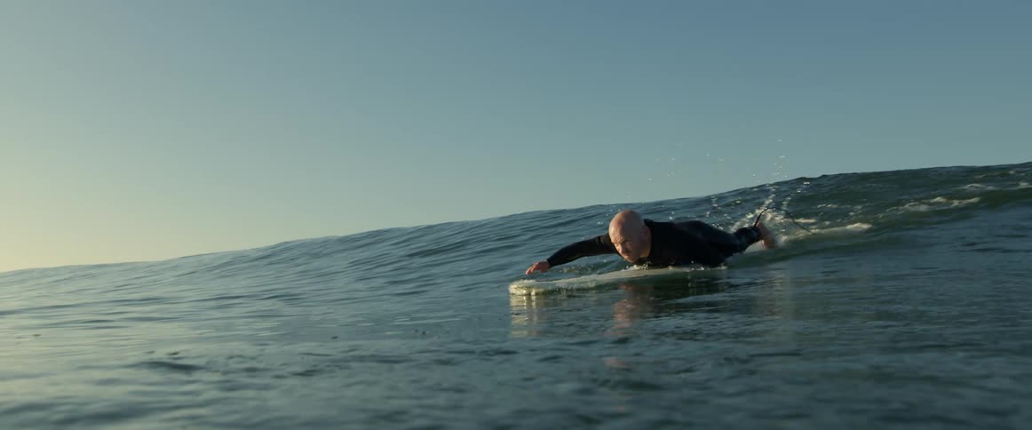 Male surfer wearing a wet suit paddles on board toward the shore before standing on board
