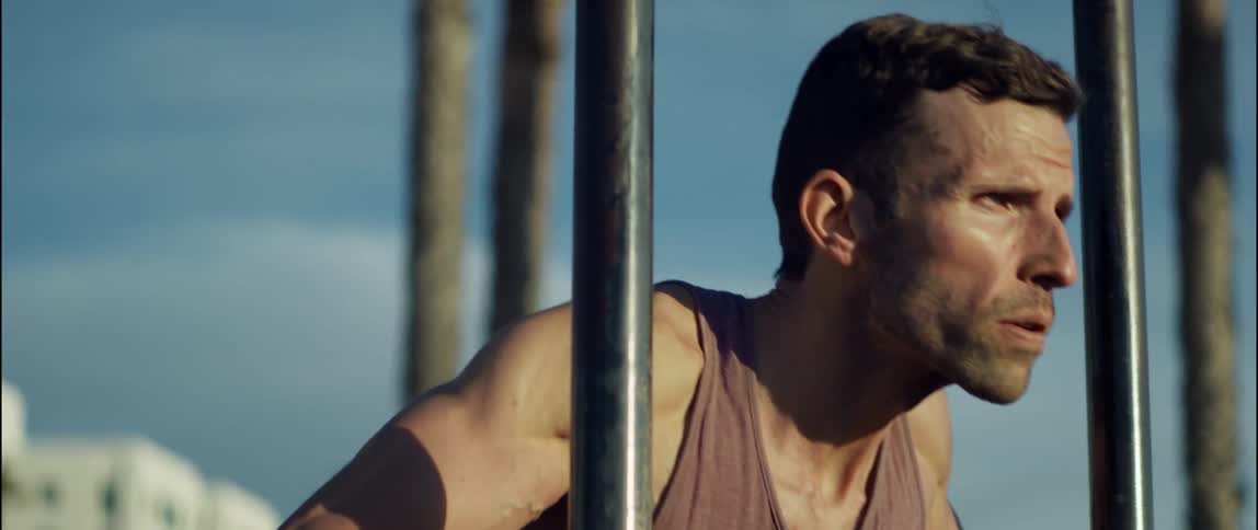 The sun shines on the face of a man outside doing exercises near metal bars