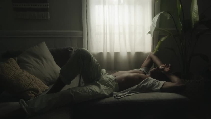 A man lies in bed with his hands covering his face