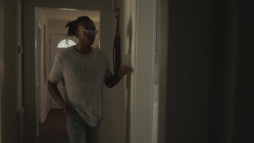 A man walks through a corridor in a house and peers through a doorway before entering a room