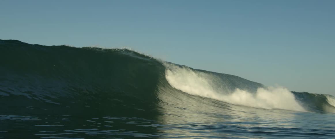 A large wave crashes in the ocean as it heads towards a beach