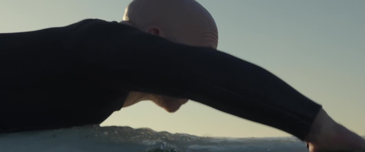 A man gets down on his board and paddles out to catch a wave