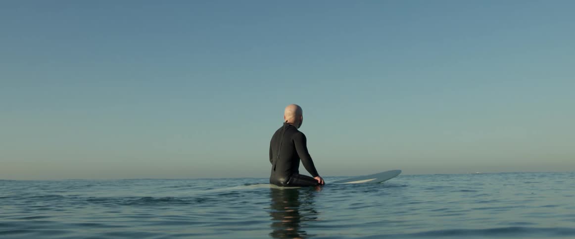 A surfer sits atop a surfboard as it floats atop the ocean during the day