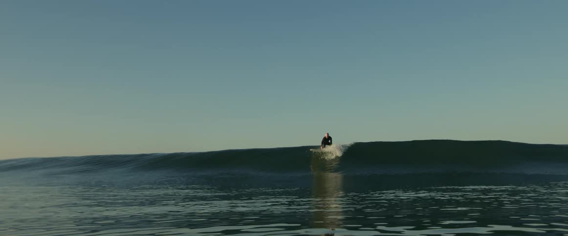 A man attempts to stand up on his surfboard as it floats before a wave on the ocean during the day