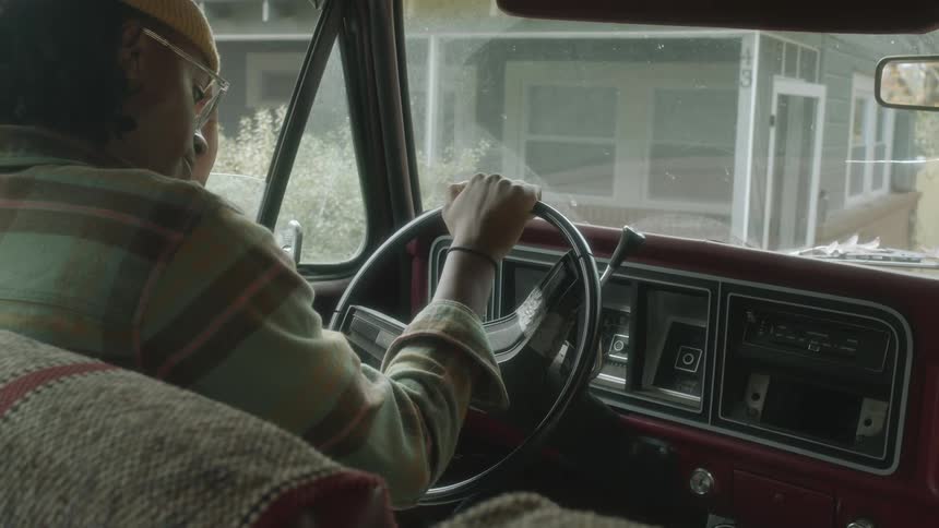 A driver sitting in a car parked in front of a house waiting and thinking