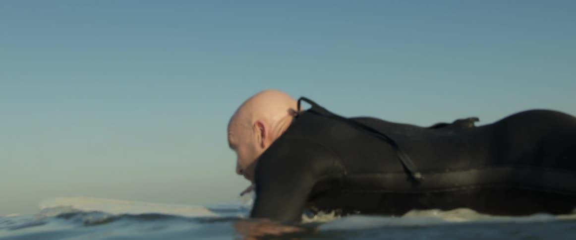 A man is paddling his surfboard out into the water