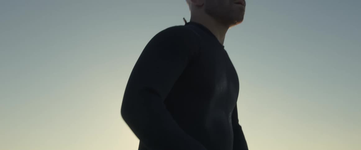 A man wearing a wet suit sitting on a surfboard looking out at the ocean