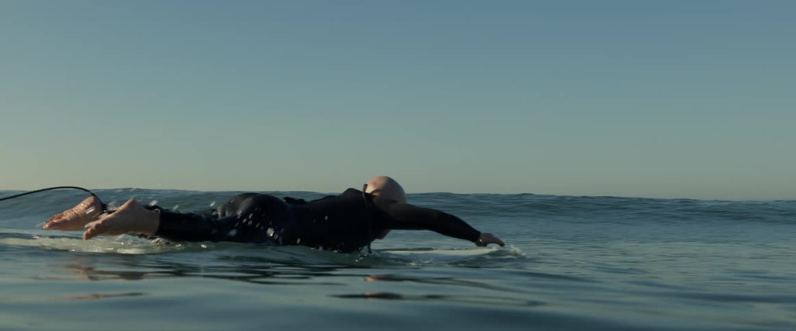 Male surfer wearing a wet suit paddles out on surfboard